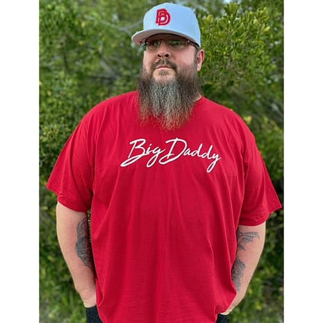 Jason_BigDaddySignatureTeeRed Man standing outside wearing a Big Daddy Signature Tee in Red and a Big Daddy Puff logo hat in white